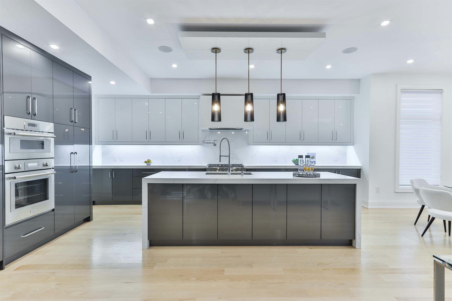 Modern grey kitchen island with three pendant lights and bespoke cabinetry by Mistry Interiors